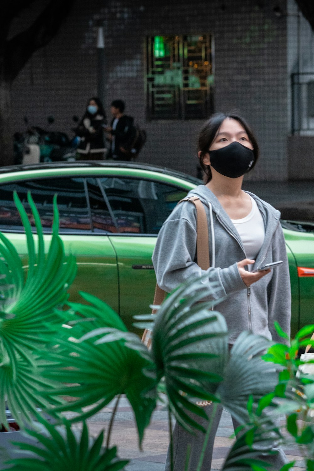 a woman wearing a face mask while standing next to a green car