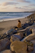 a woman sitting on rocks on the beach