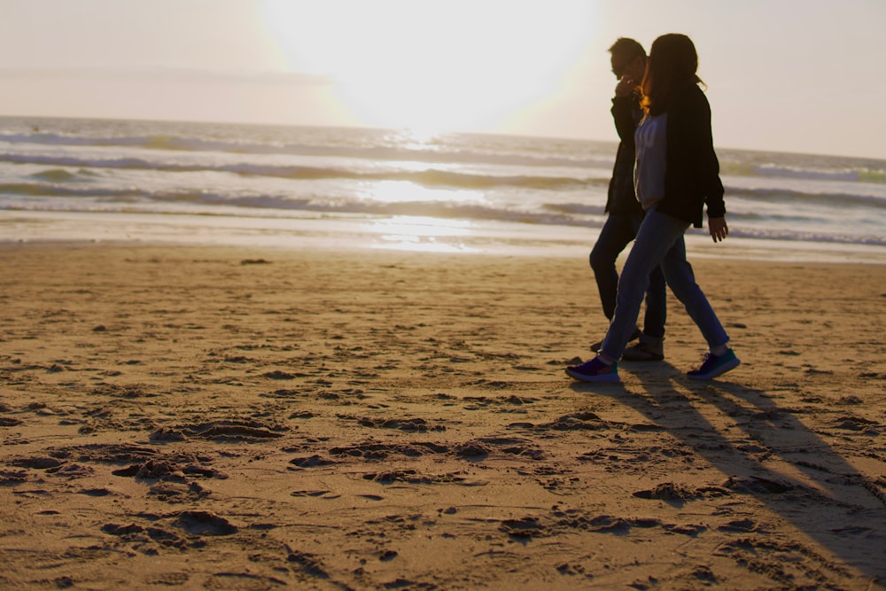 two people walking on a beach near the ocean