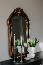 a mirror sitting on top of a dresser next to a vase with flowers