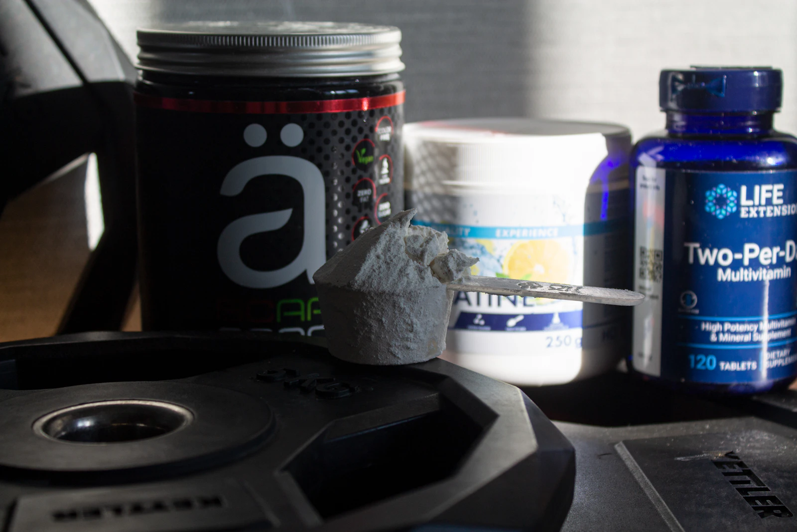 Supplement jars and a scoop on a gym surface.