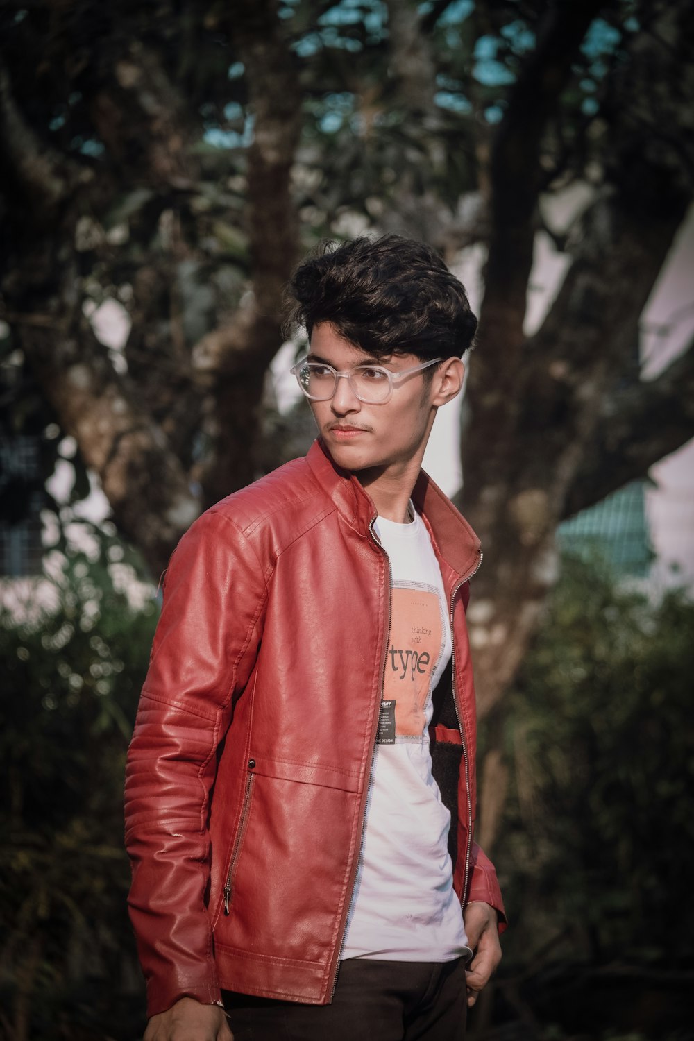 a man in a red leather jacket standing in front of a tree