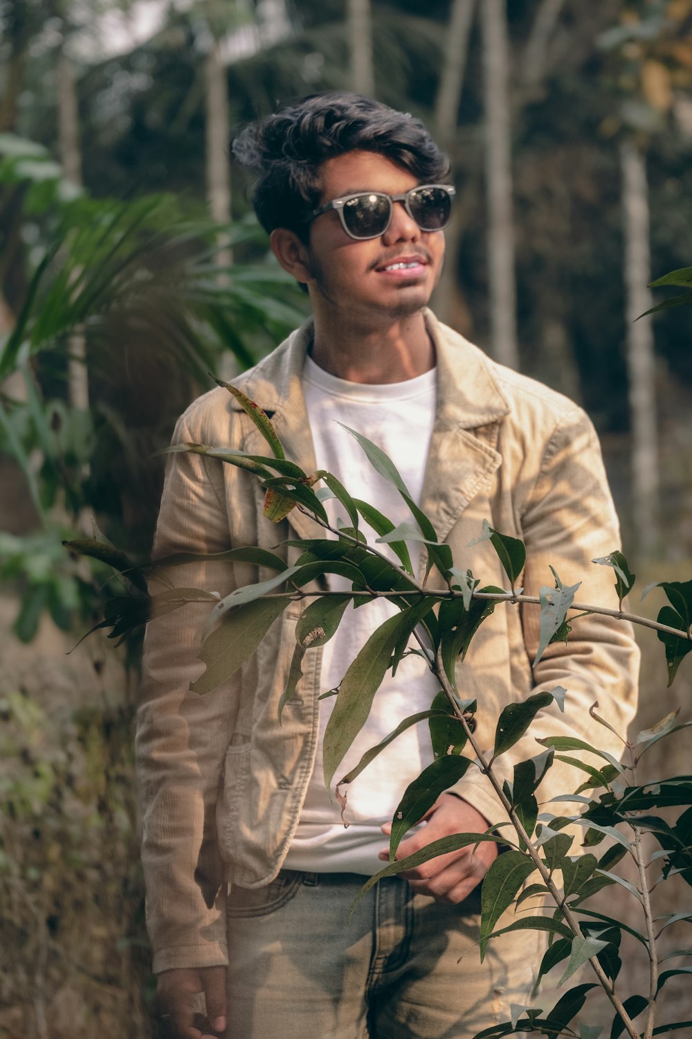 a man wearing sunglasses standing next to a tree