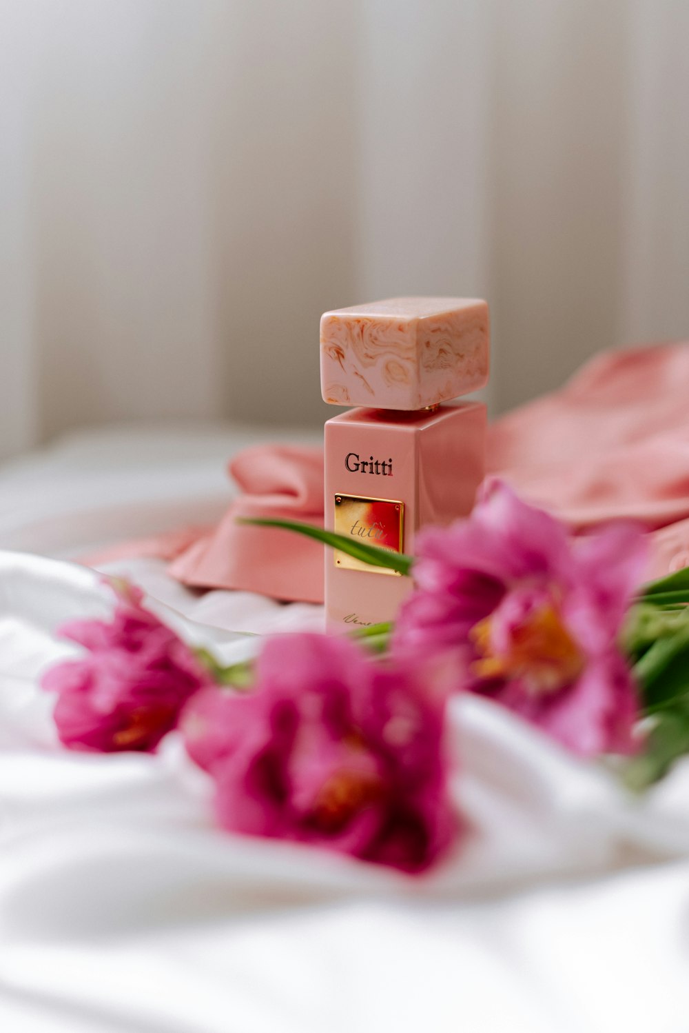 a bottle of perfume sitting on top of a bed next to pink flowers