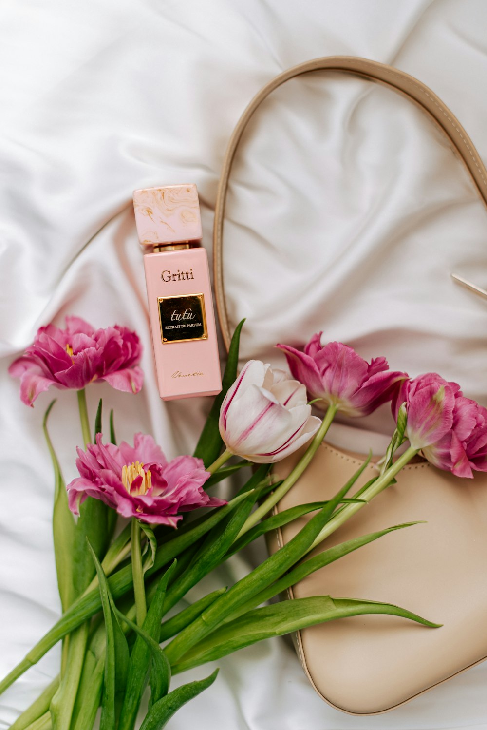 pink flowers and a bottle of perfume on a white bed