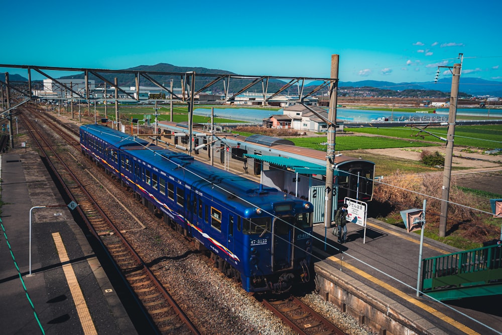 um trem azul viajando pelos trilhos do trem ao lado de um campo verde exuberante