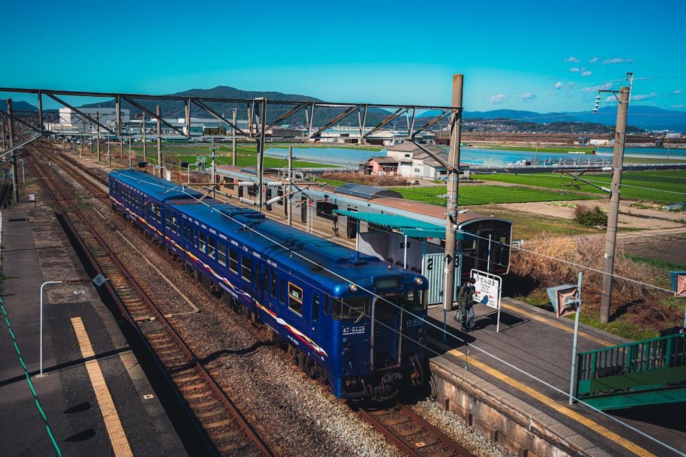 a blue train traveling down train tracks next to a lush green field