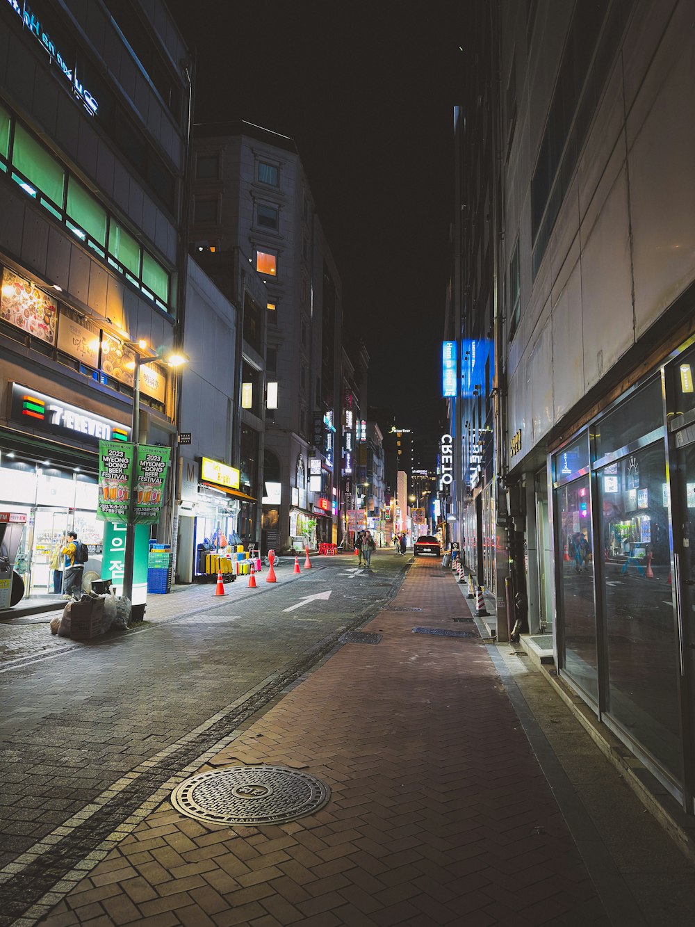 una calle de la ciudad por la noche con edificios y una persona durmiendo en la acera