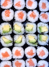 a tray of sushi with avocado and salmon