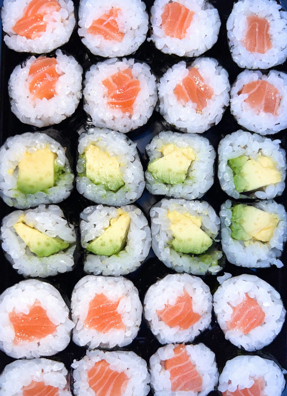 a tray of sushi with avocado and salmon