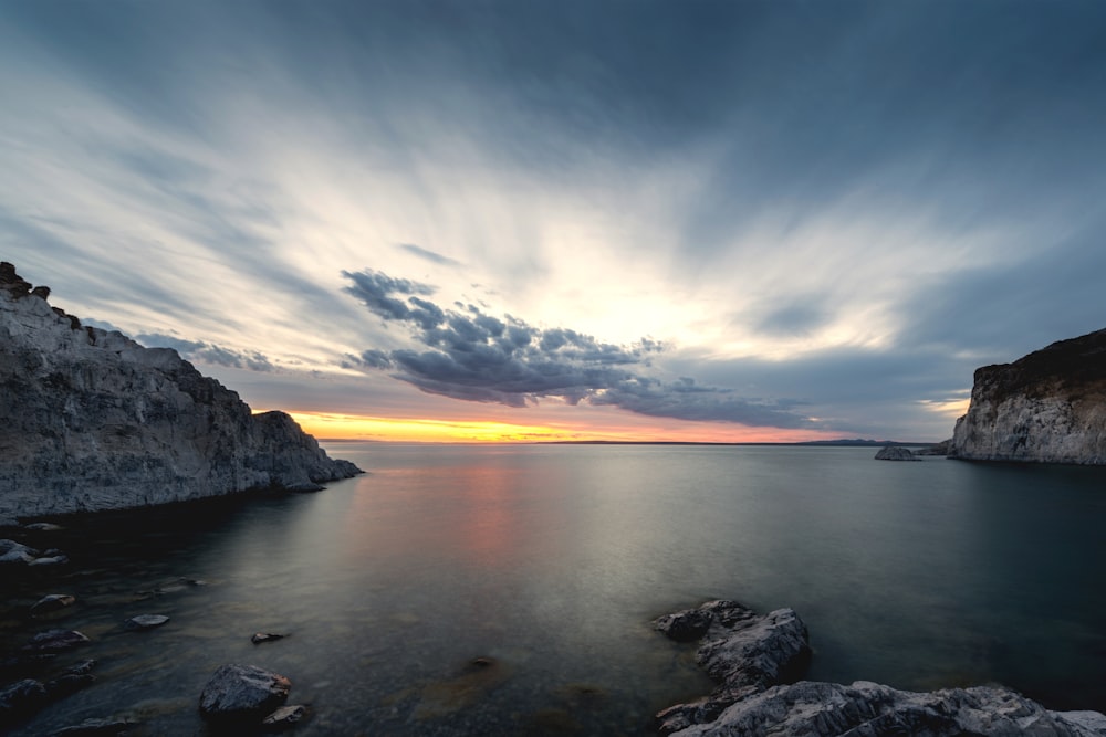 the sun is setting over the water and rocks