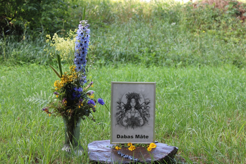 a memorial sits in the grass next to a vase with flowers