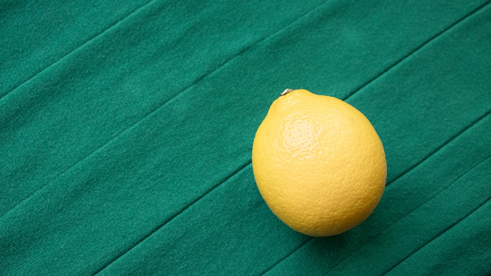 a single lemon sitting on a green cloth