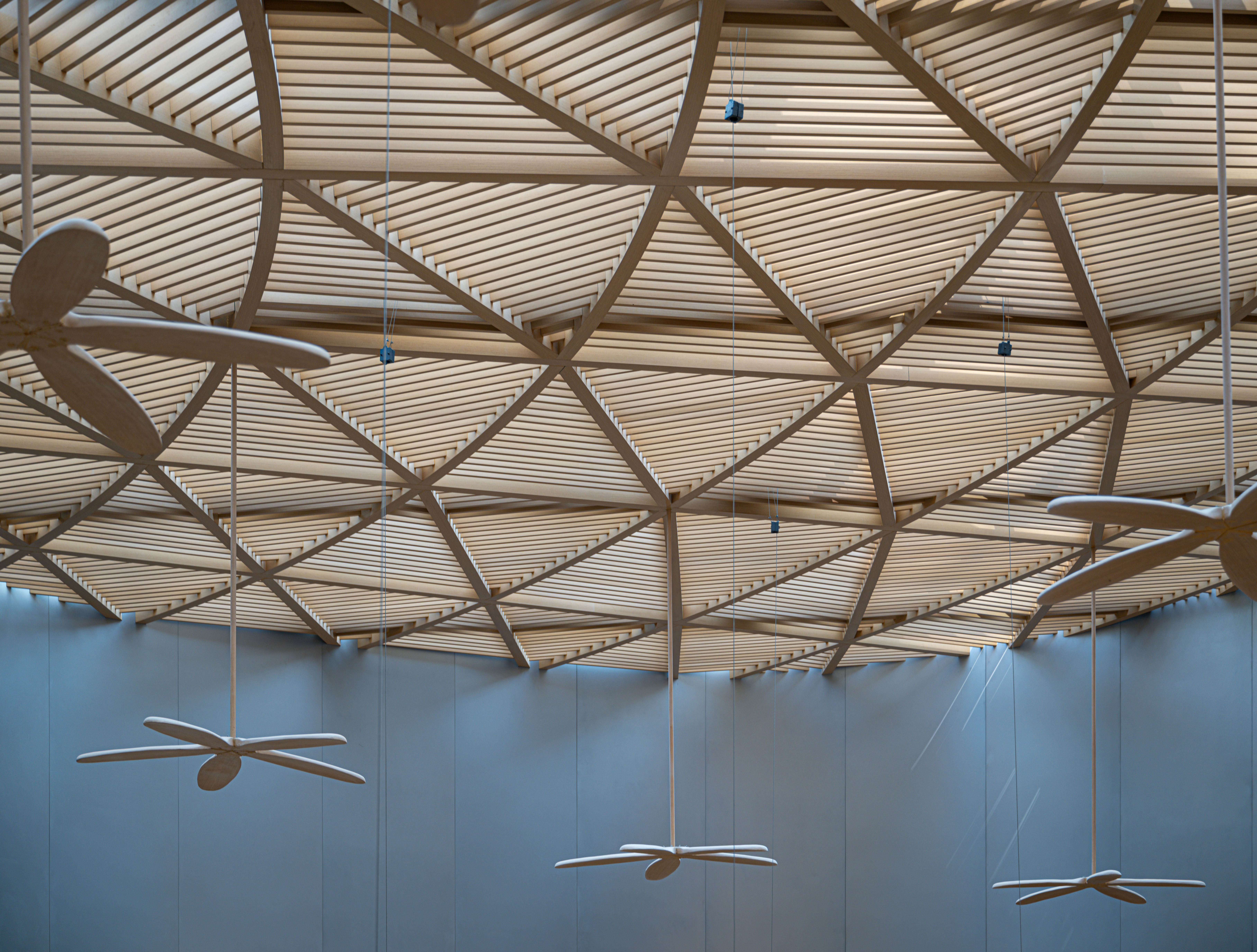 Geometric wooden slat ceiling with suspended propeller-shaped decorative fixtures in modern interior space