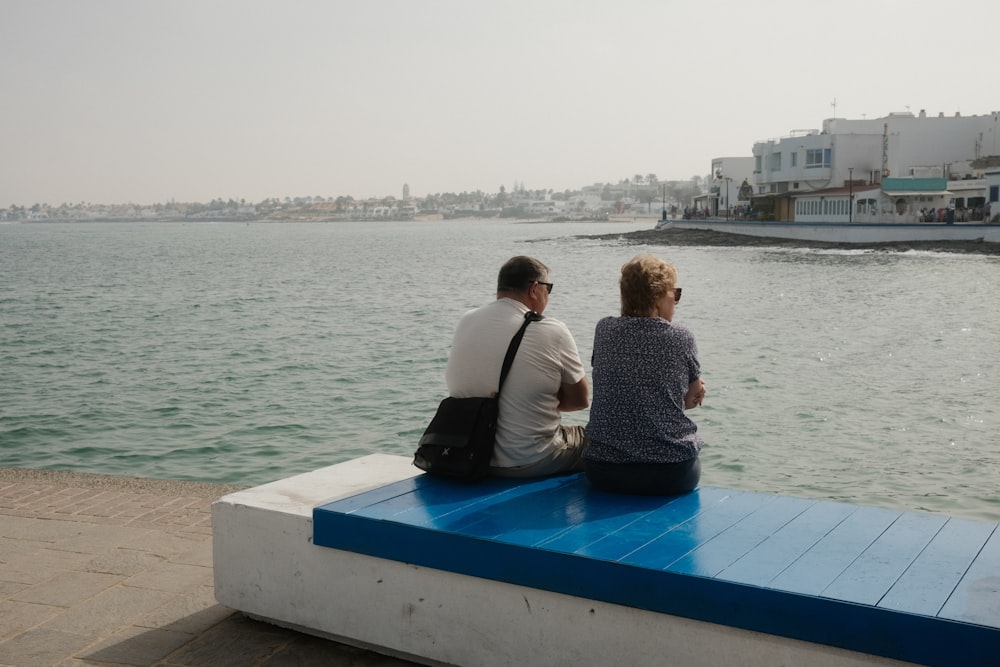 a man and a woman sitting on a bench looking out at the water