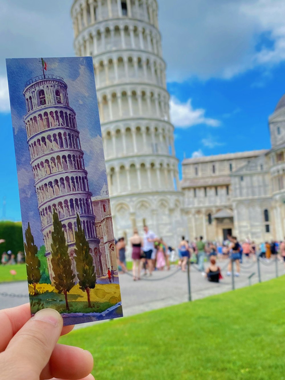a hand holding up a picture of a leaning tower
