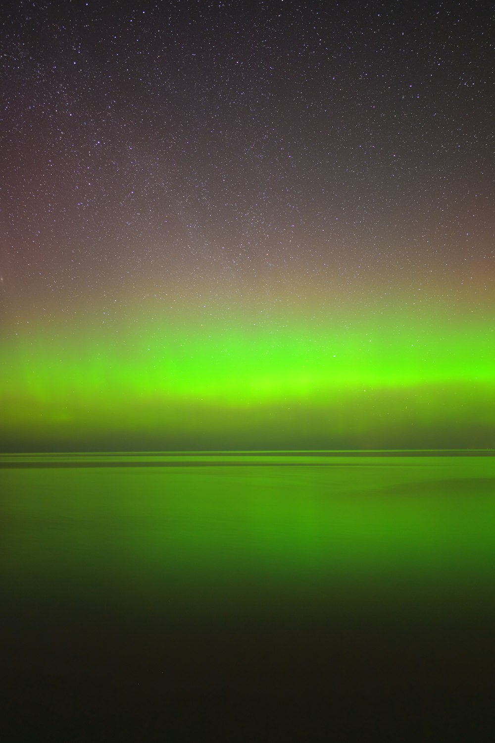 a green and purple sky with stars above the water