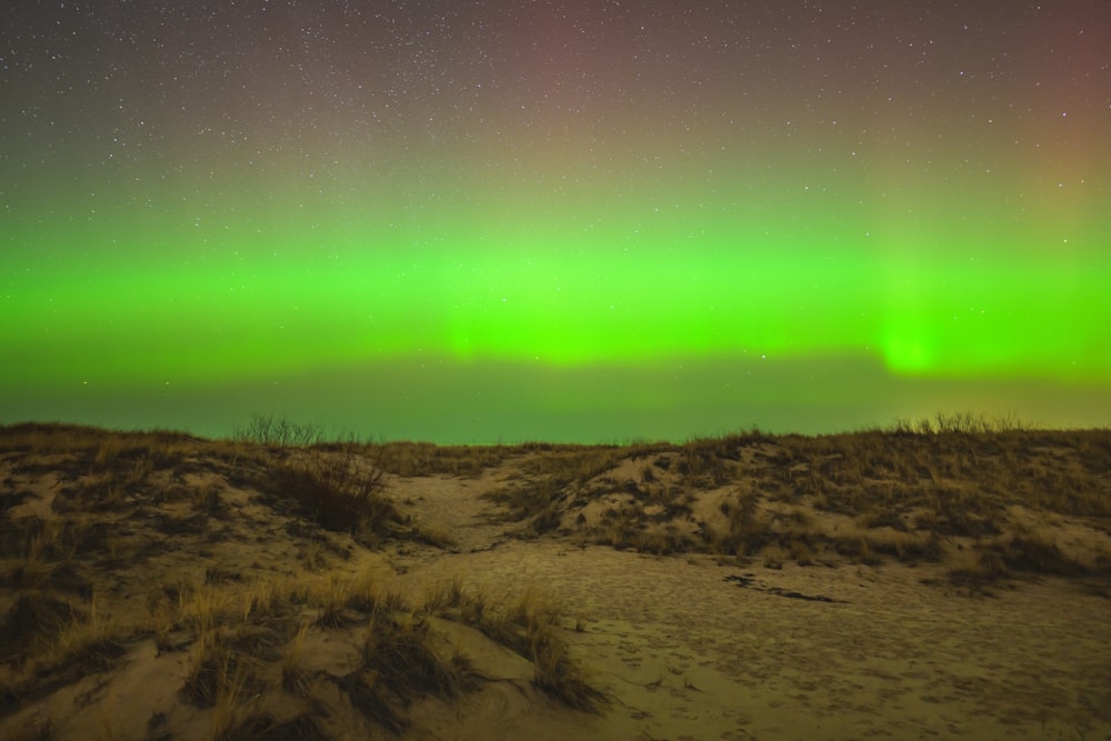 a green and red aurora over a sandy area