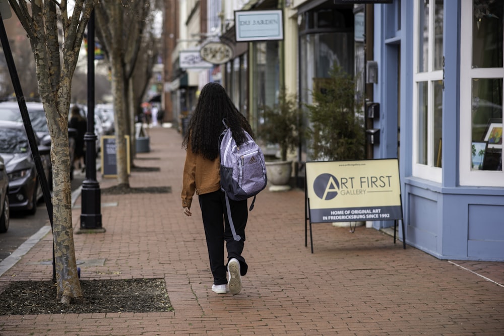 a woman walking down a sidewalk carrying a purple bag