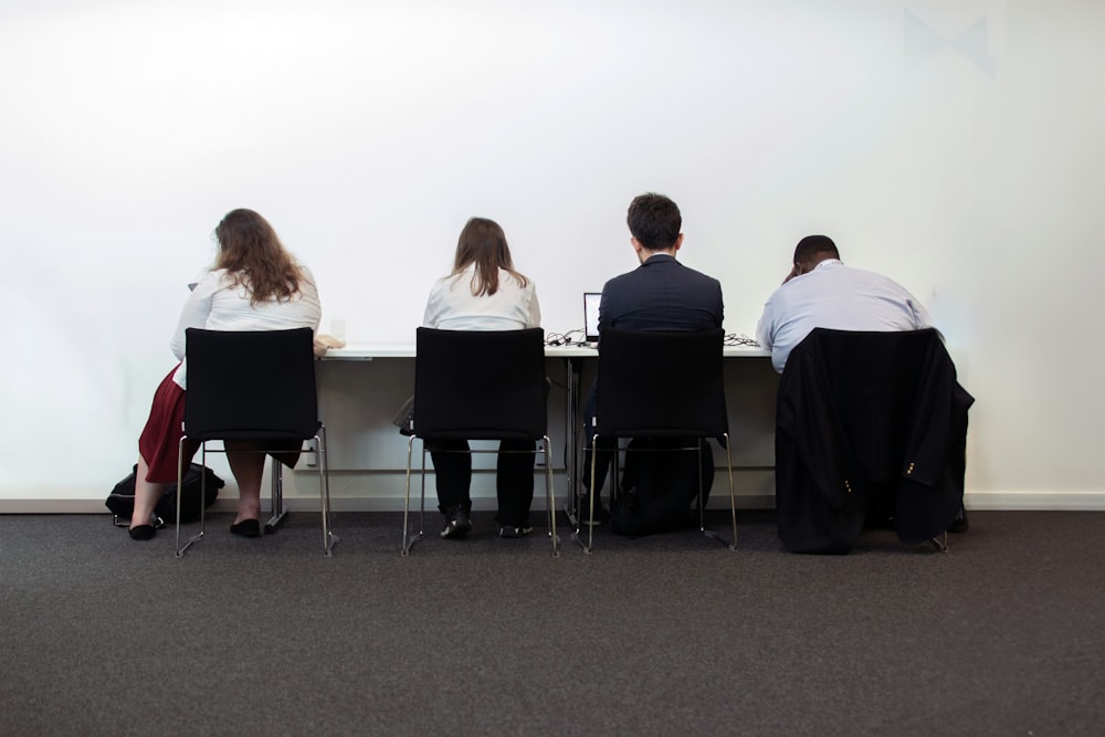 a group of people sitting at a table in front of a white wall