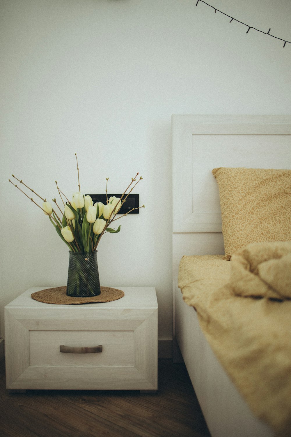 a vase of flowers sitting on a nightstand next to a bed