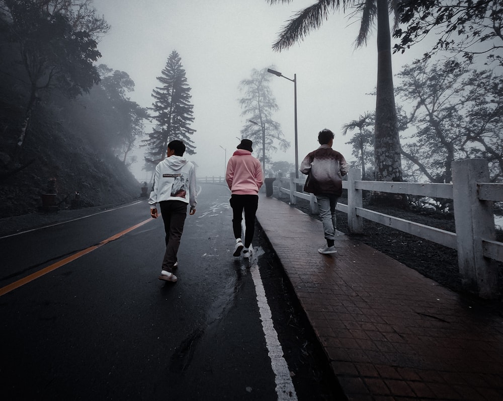 three people walking down a road in the rain