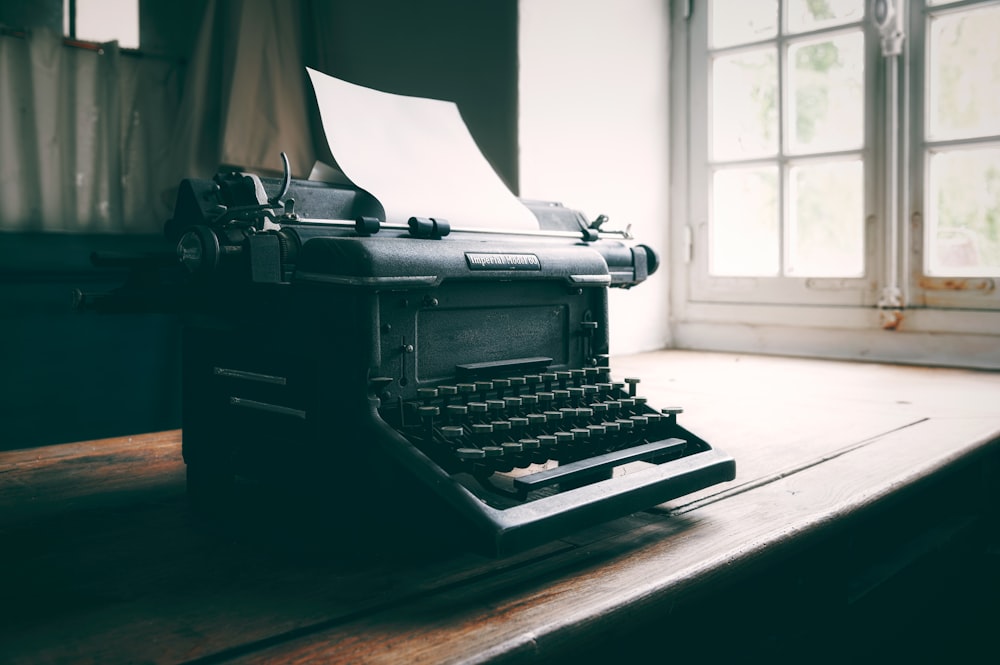 uma máquina de escrever à moda antiga sentada em uma mesa em frente a uma janela