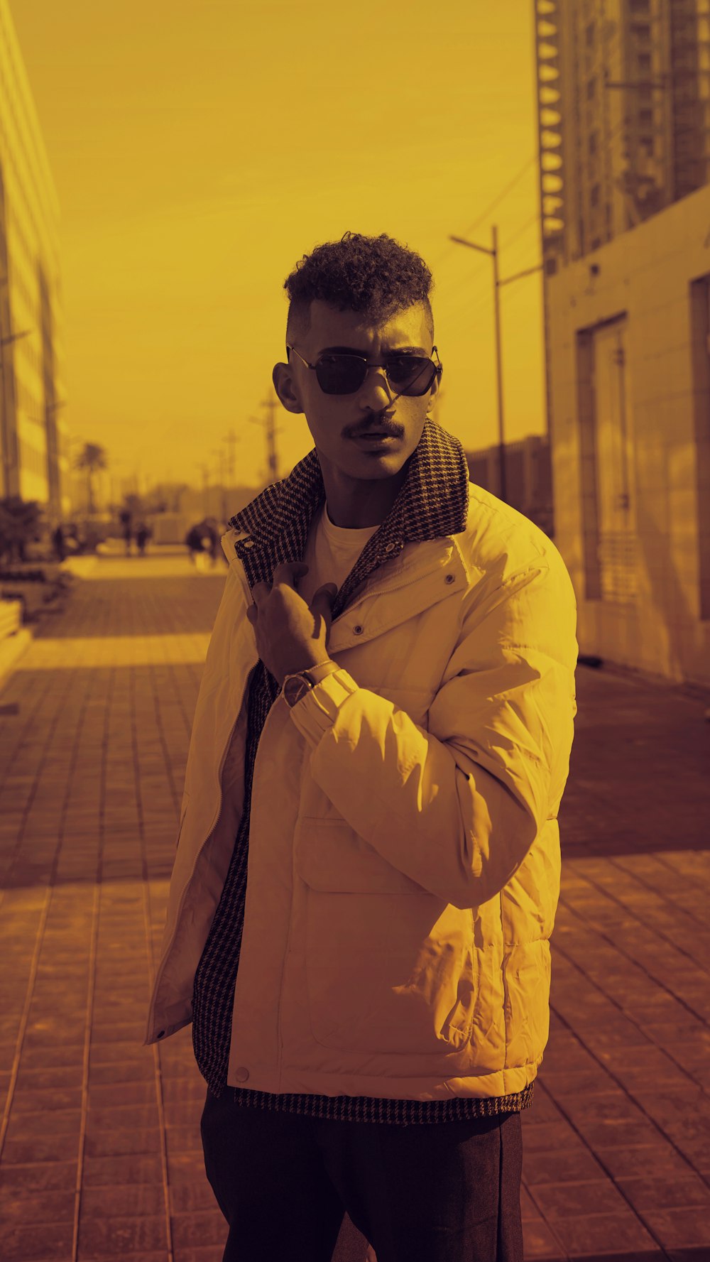 a man in a jacket and sunglasses standing on a sidewalk