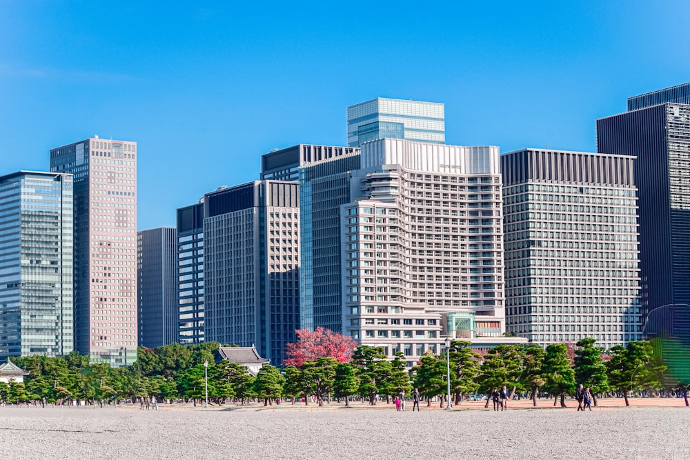 a group of people walking on a beach in front of tall buildings