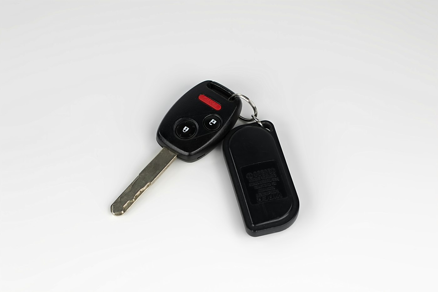 A remote head car key and a keyring fob on a plain background.