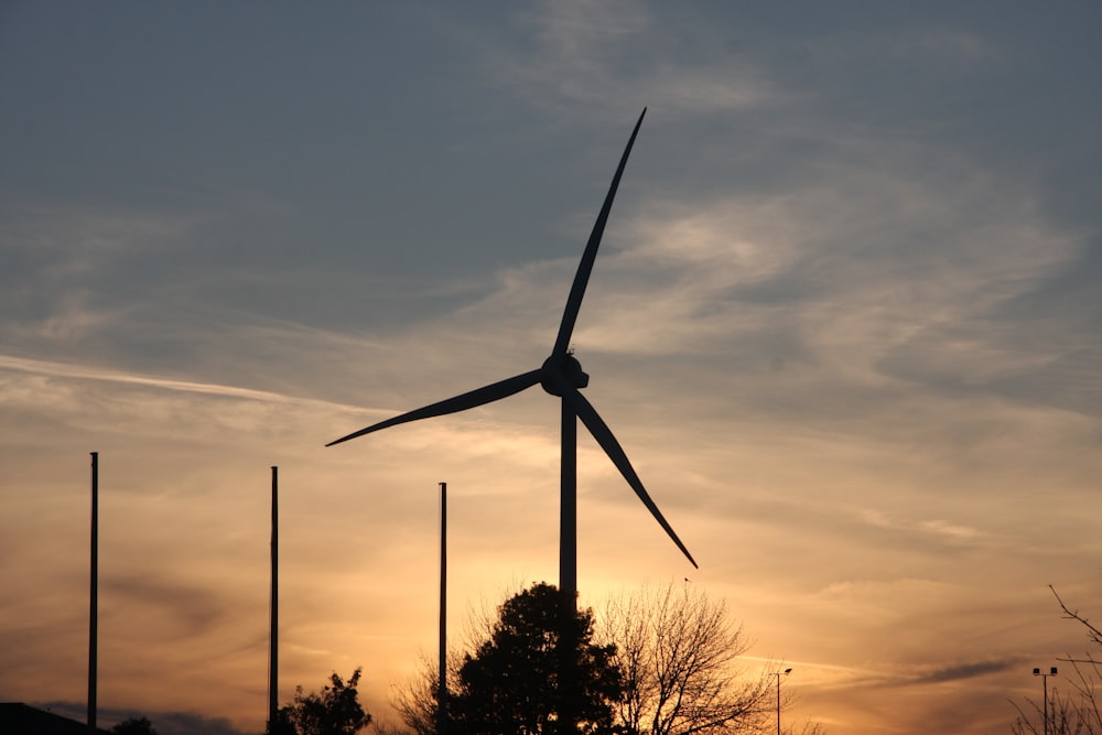 the sun is setting behind a wind turbine