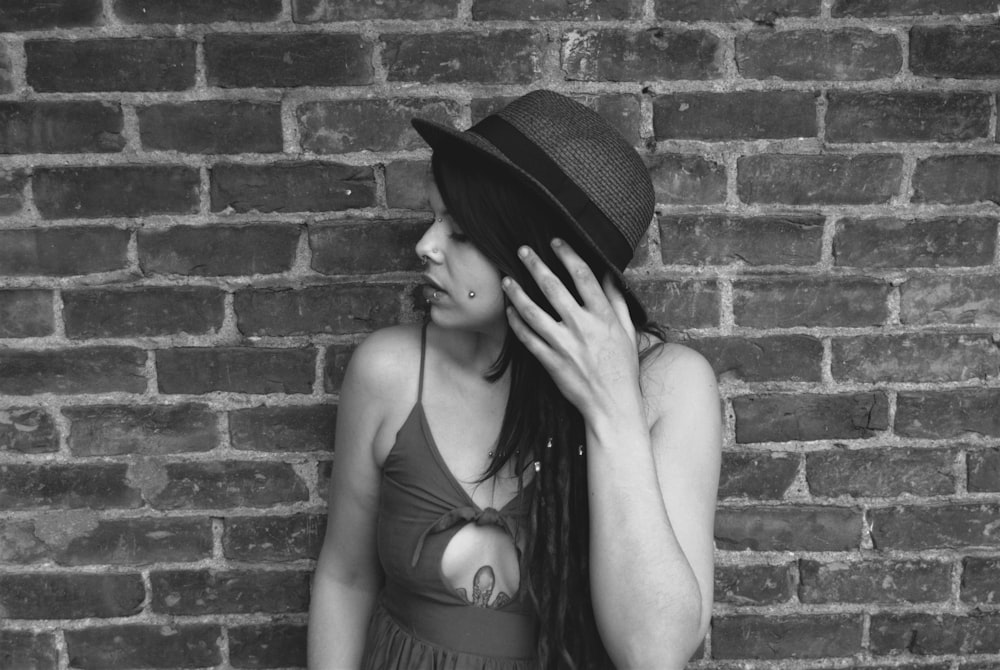 a woman wearing a hat standing in front of a brick wall