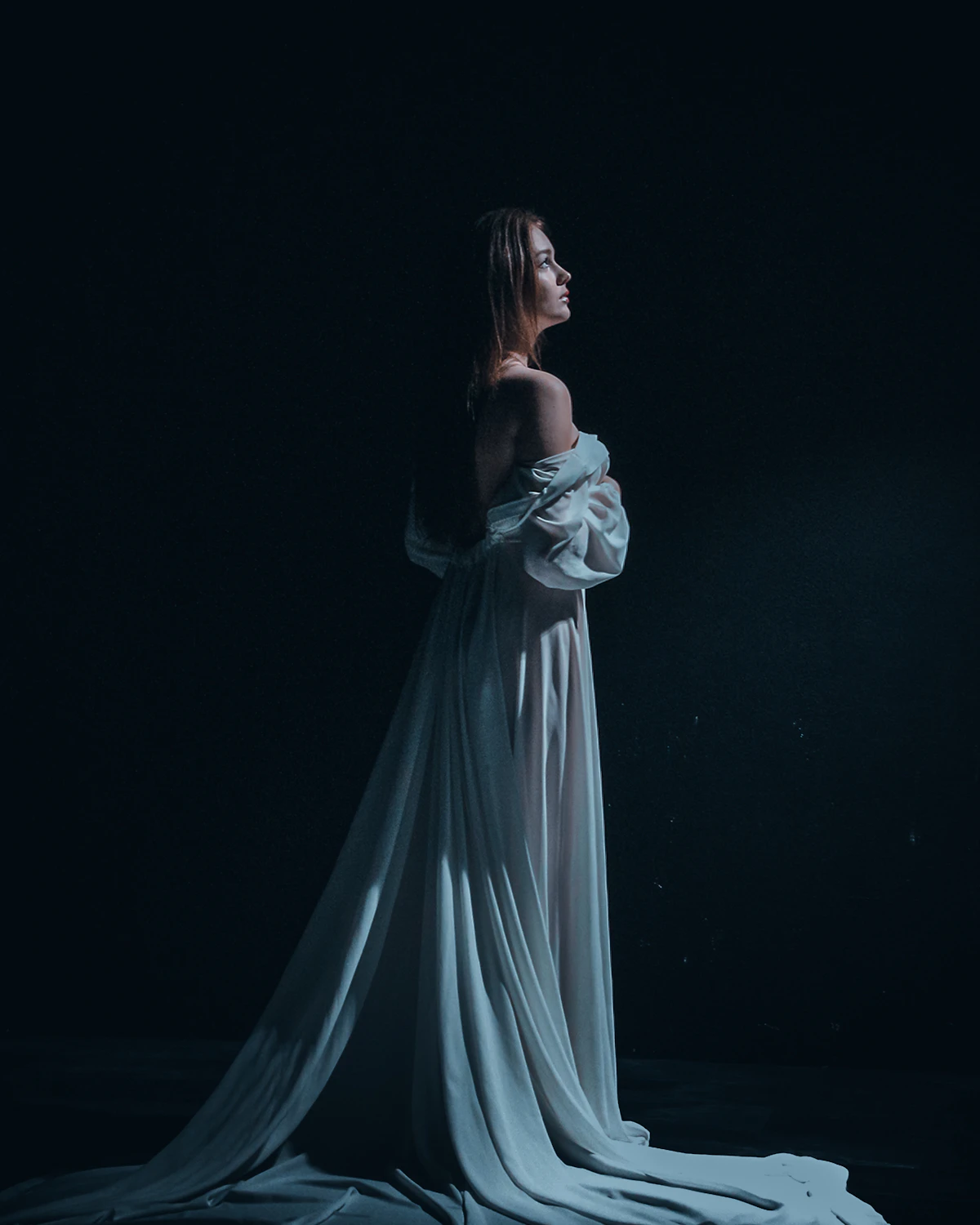 Woman in a flowing white gown against a dark studio backdrop