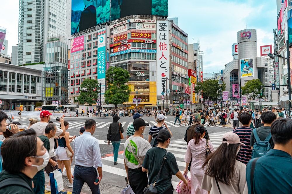 a crowd of people walking across a street next to tall buildings