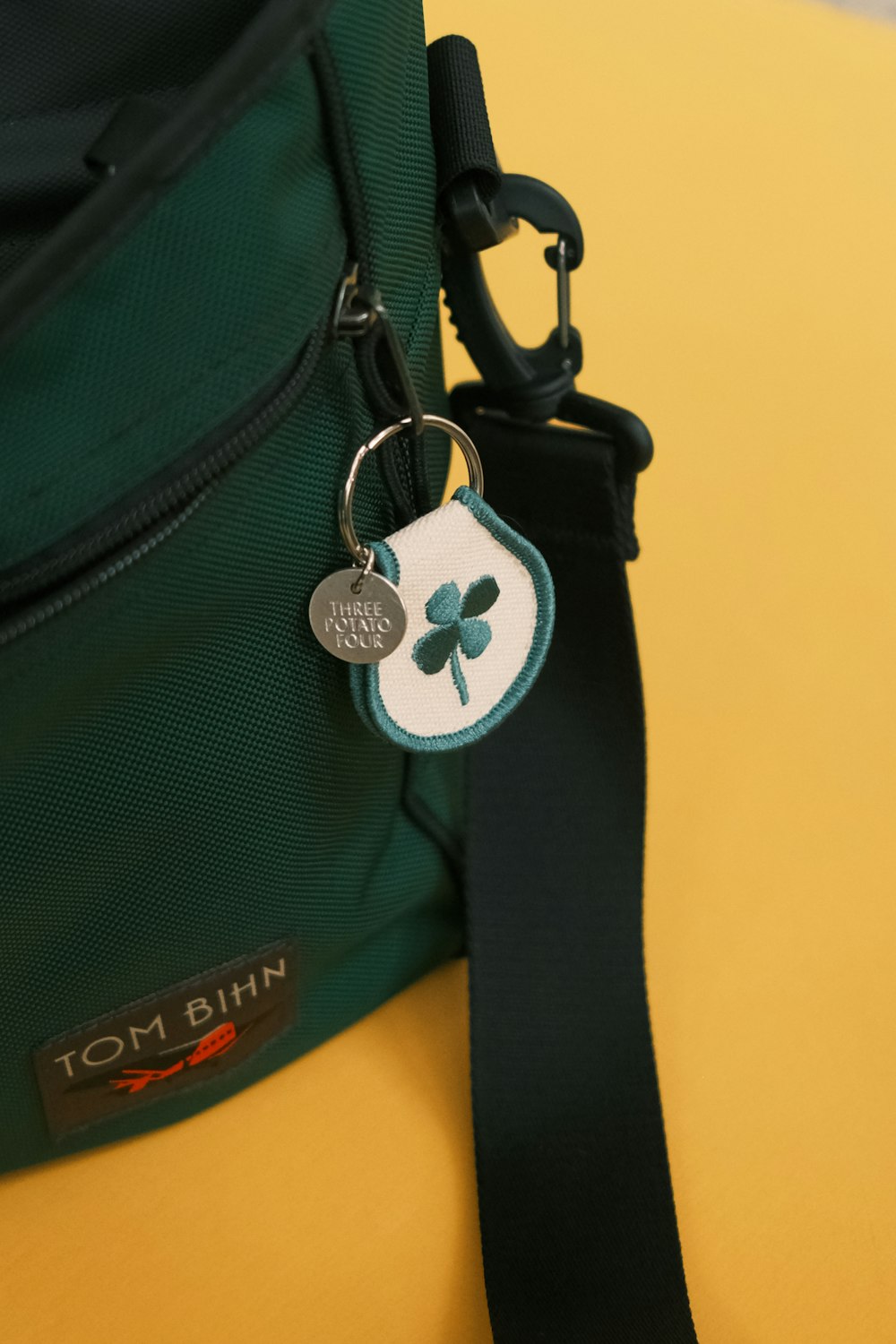 a green bag with a black strap and a clover keychain