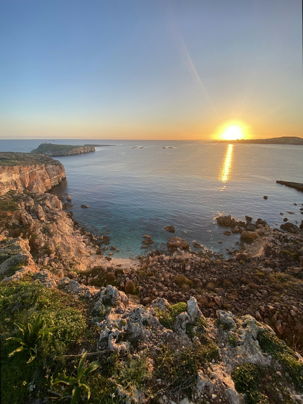 the sun is setting over the ocean and rocky shore