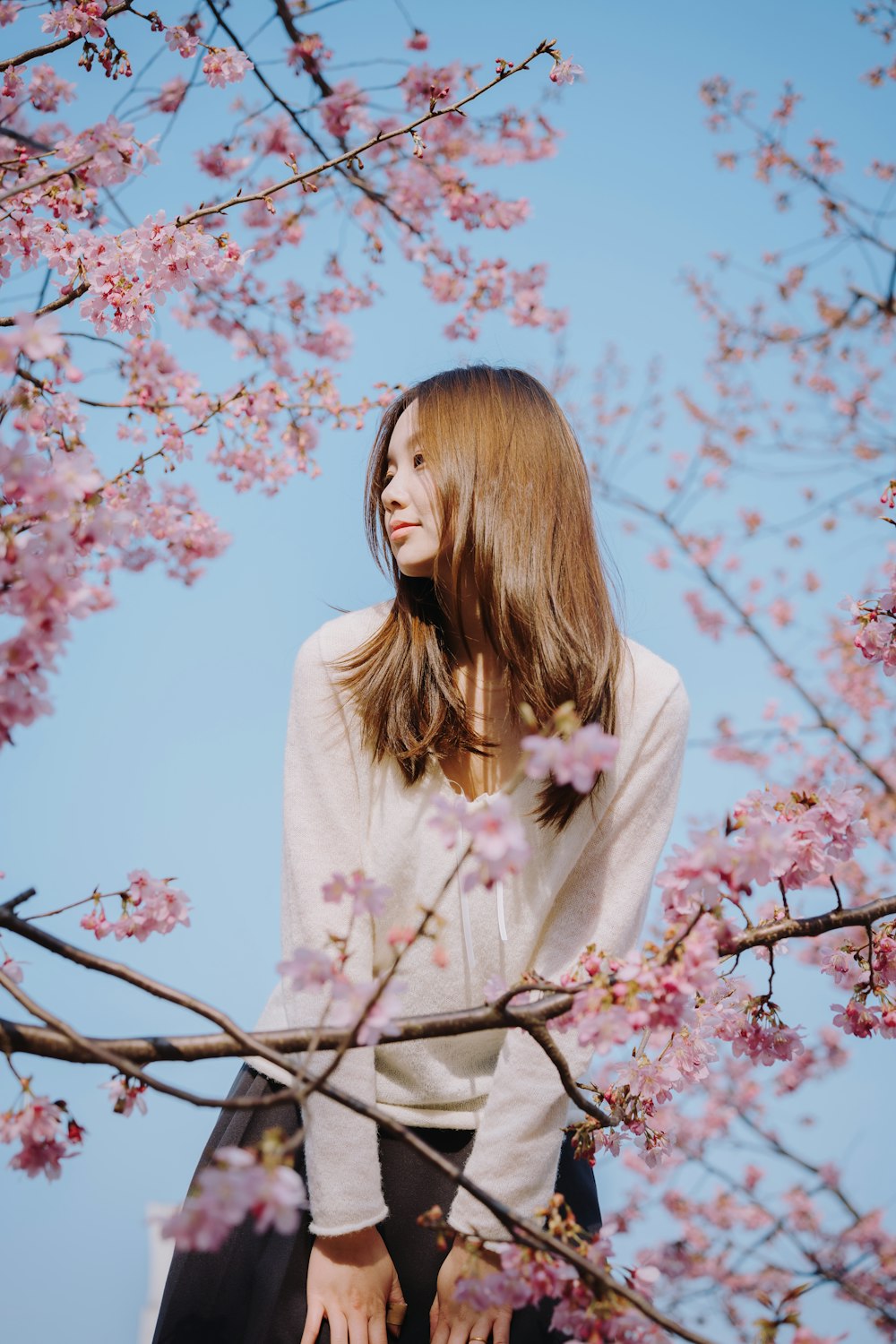 a woman standing in front of a tree with pink flowers