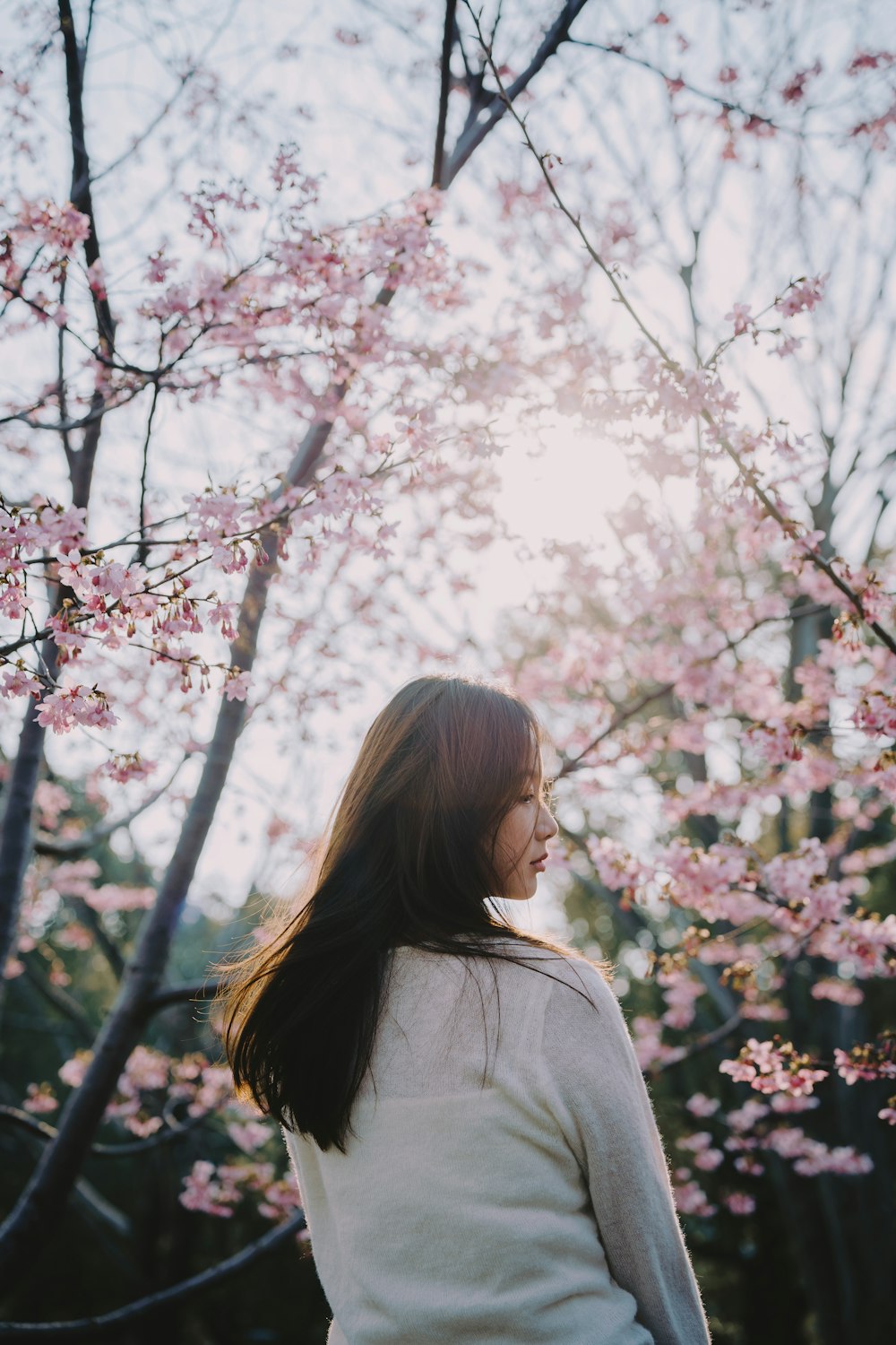 a woman standing in front of a tree with pink flowers