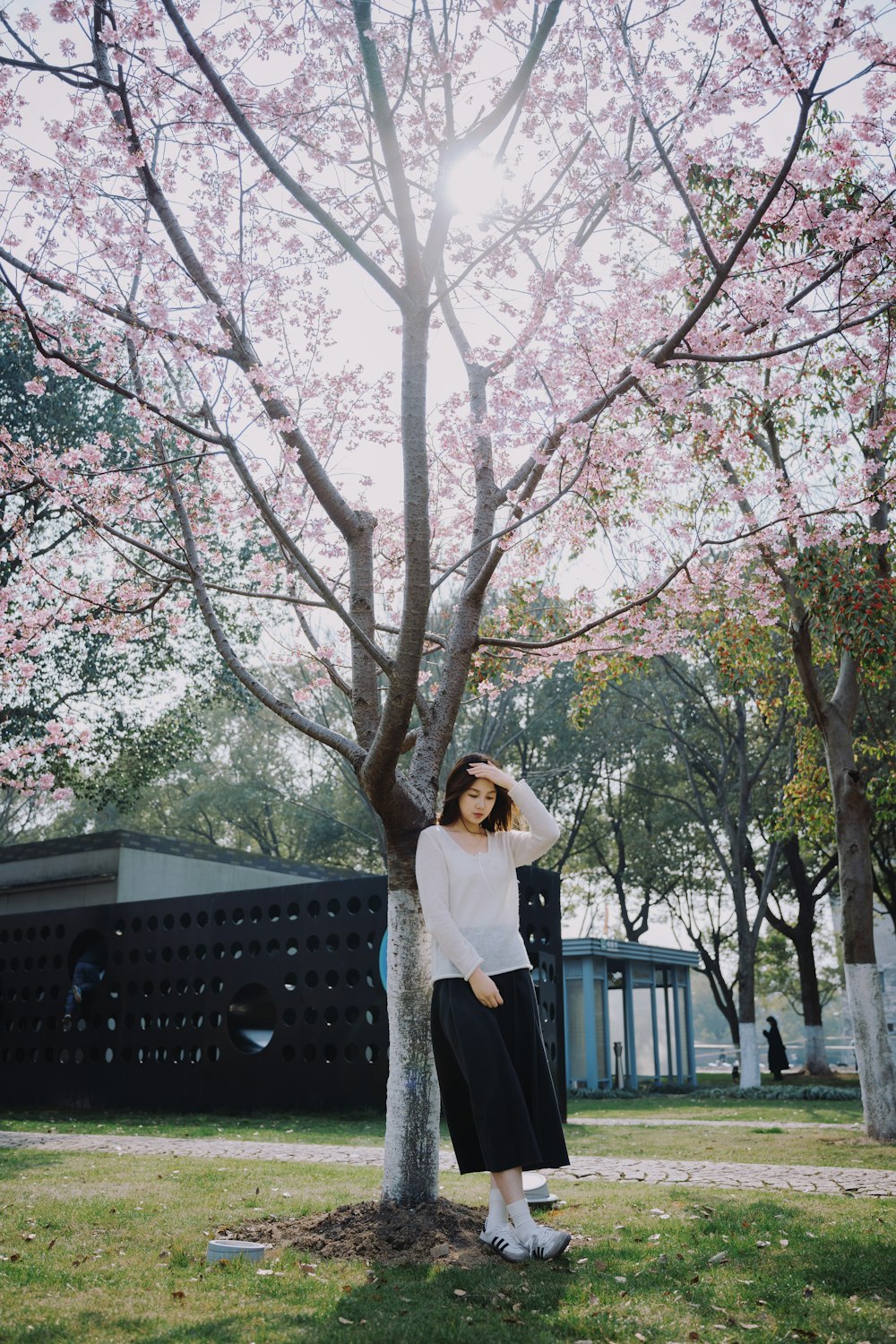 a woman standing next to a tree with pink flowers