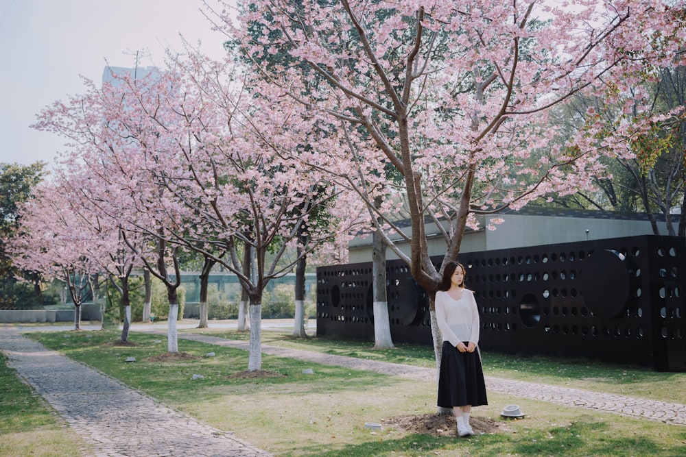 a woman standing in front of a tree with pink flowers