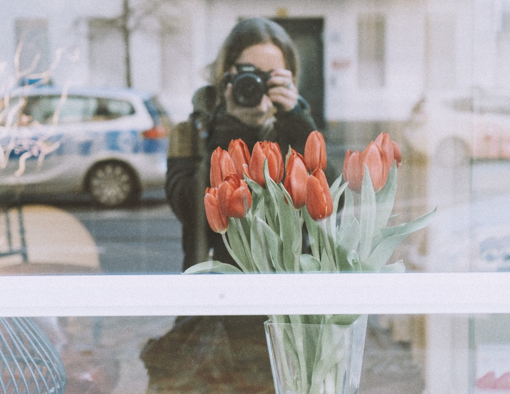 a woman taking a picture of a vase of flowers