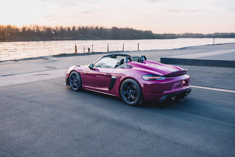 a purple sports car driving down a road next to a body of water