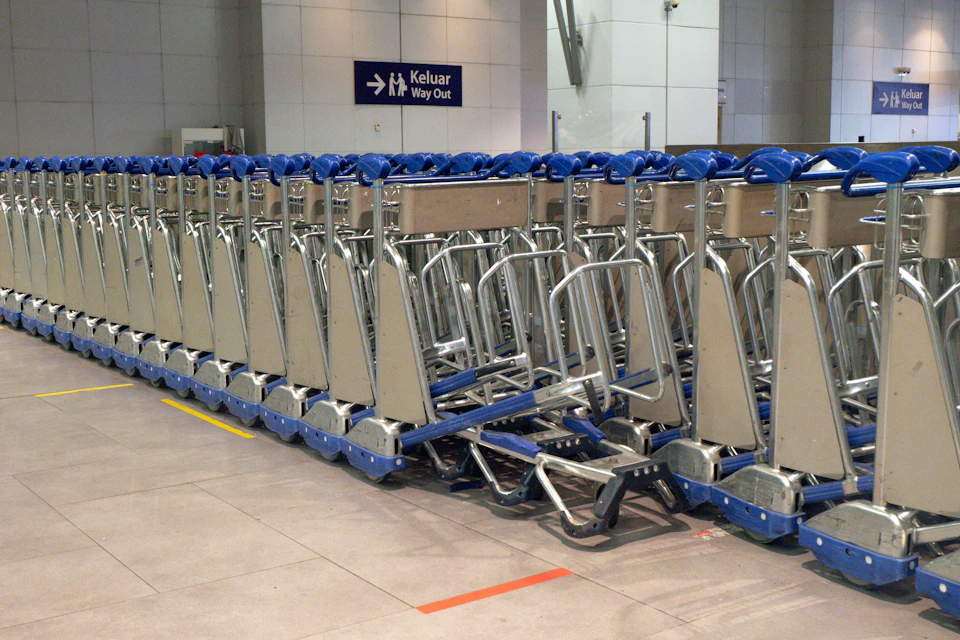 Row of silver luggage carts line up against a white wall with destination signs