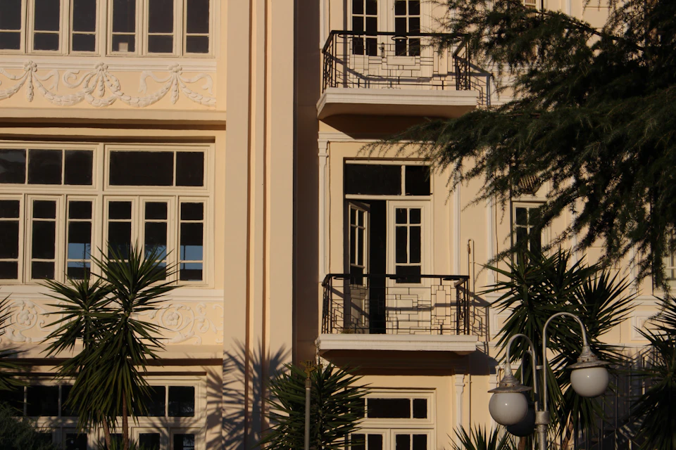 Two-story white building with black railings on a street corner with surrounding palm trees