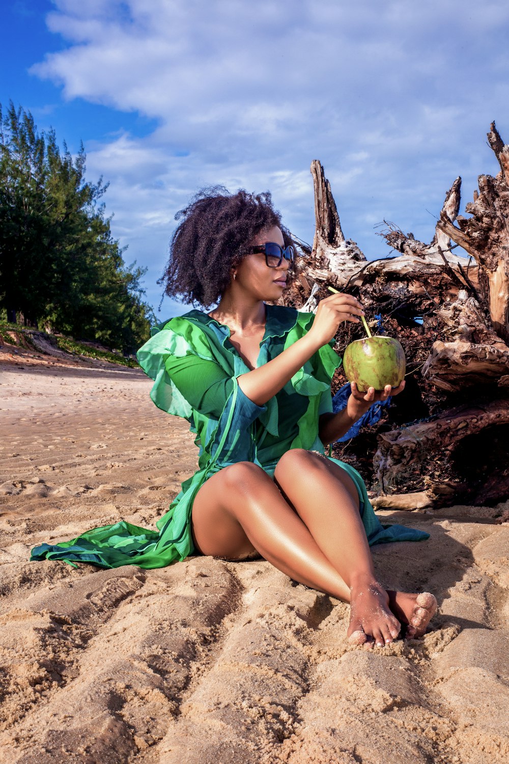 a woman sitting on a beach holding a coconut
