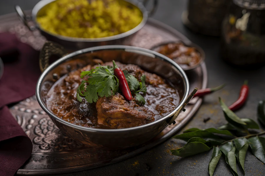 A lamb curry in a copper bowl with fresh chilli and curry leaves