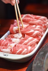 a person holding chopsticks over a tray of raw meat