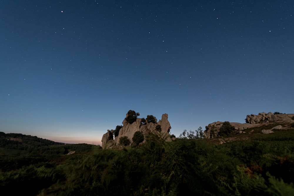 a night sky with stars above a rocky outcropping