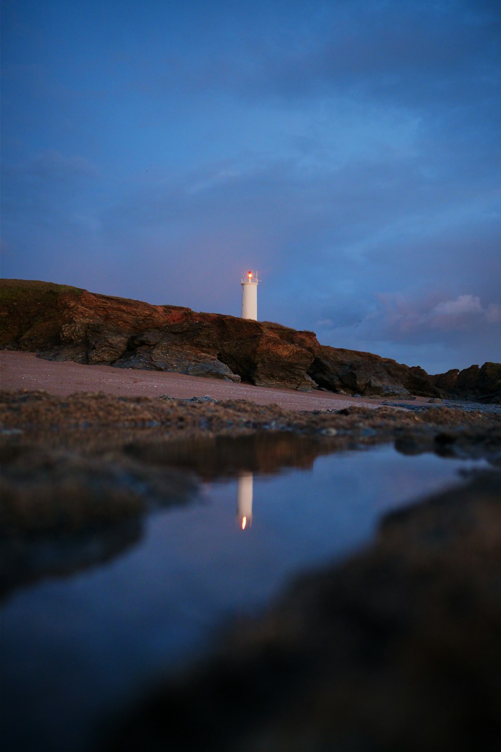 un faro seduto in cima a una collina accanto a uno specchio d'acqua