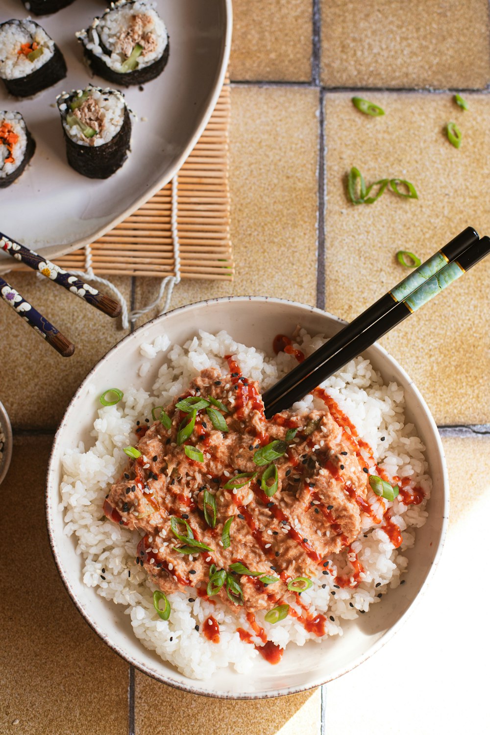 a bowl of rice with chopsticks and a plate of sushi